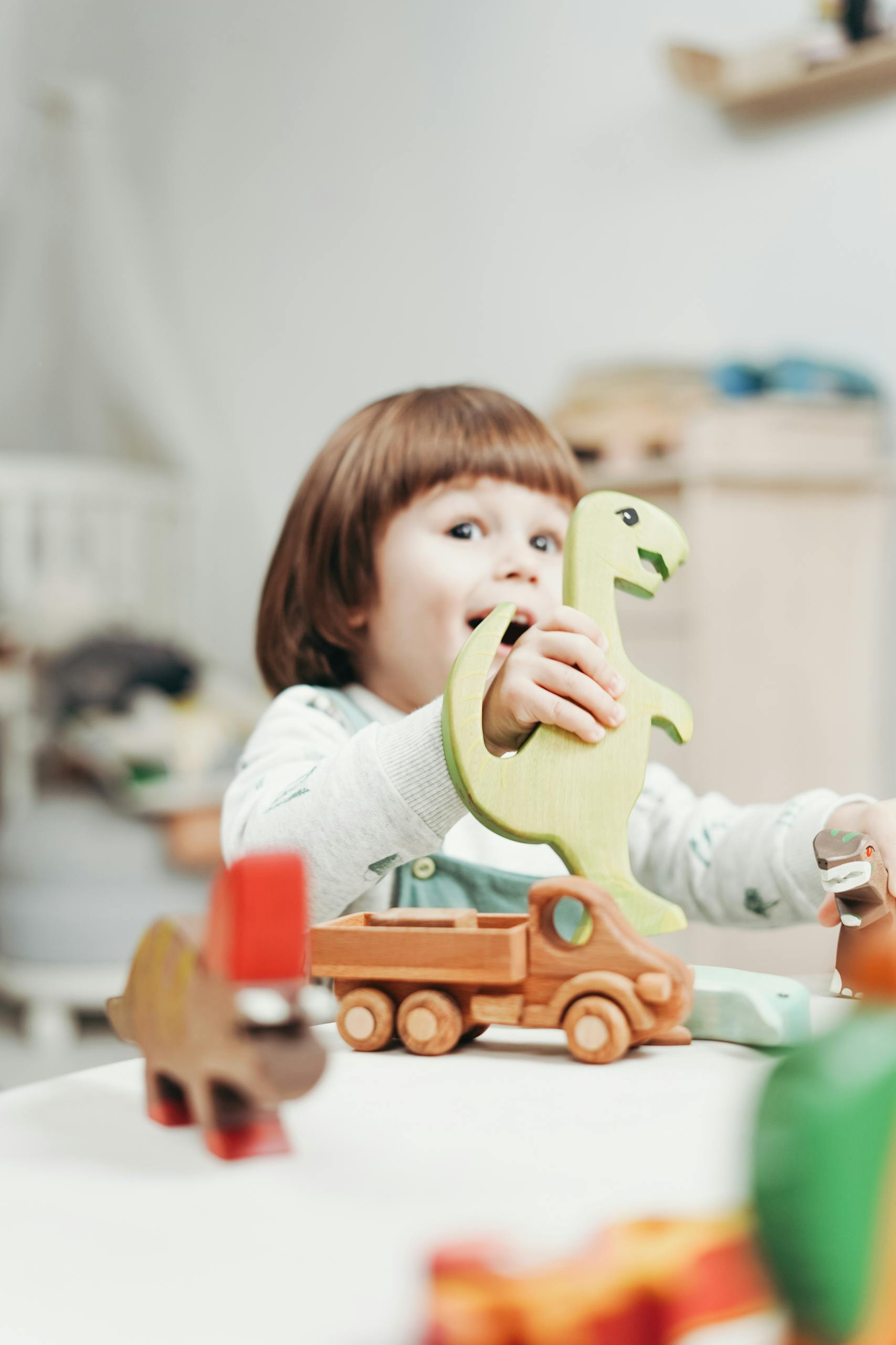 A cheerful child engages in imaginative play with wooden dinosaur toys indoors.